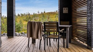 Een houten terras met een tafel, stoelen, een bankje en uitzicht op een glooiend landschap.