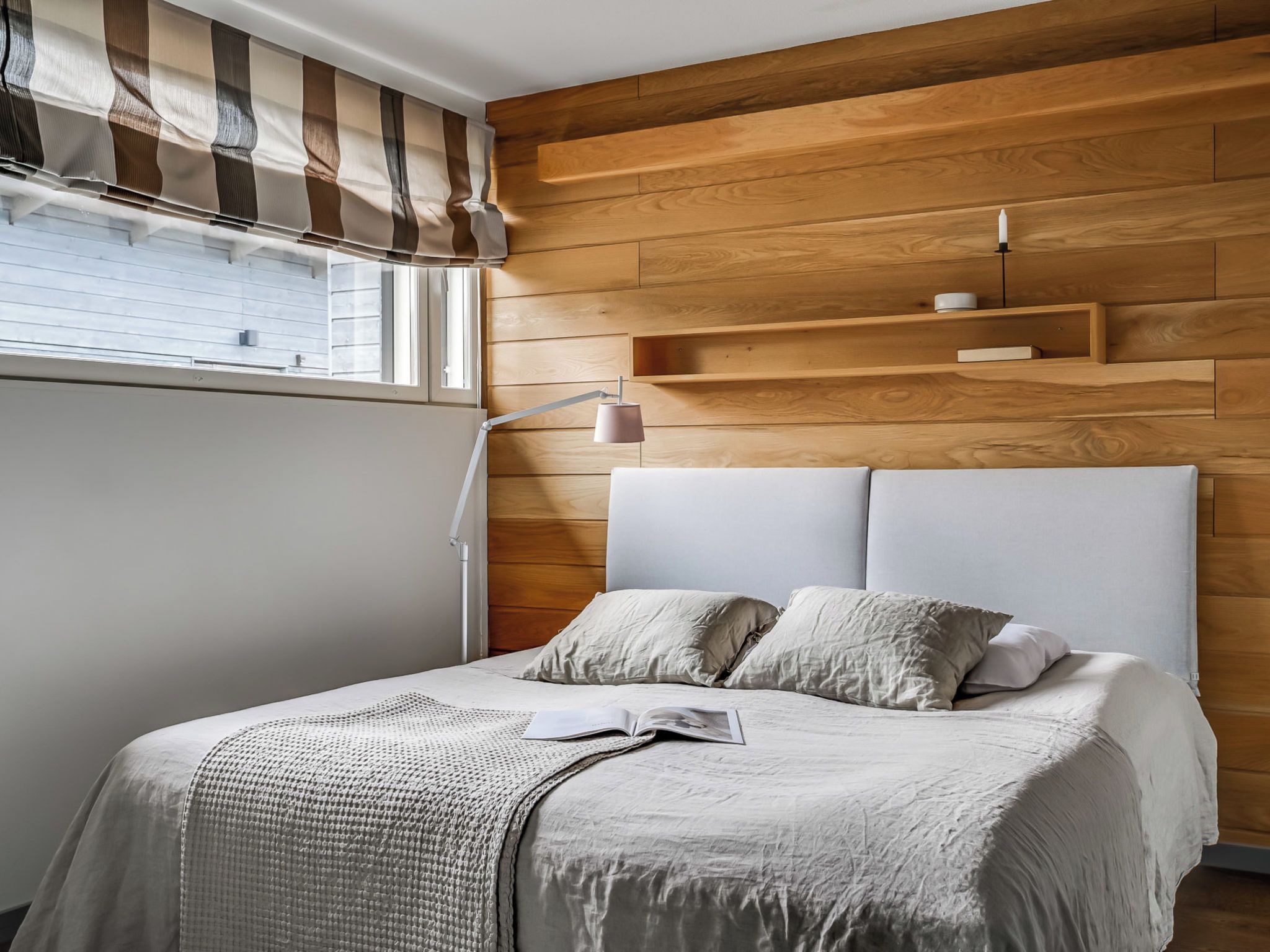 A bedroom with a bed, a bedside lamp, and a window with blinds.