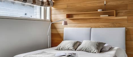 A bedroom with a bed, a bedside lamp, and a window with blinds.