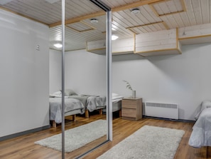 A modern bedroom with a glass partition, wooden flooring, a bed with a grey blanket, a bedside table with a lamp, and a white radiator.