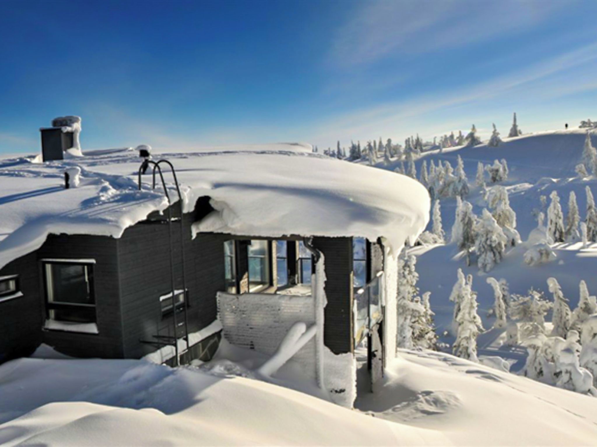 A snow-covered building with a large window, a chimney, and a snow-covered roof.