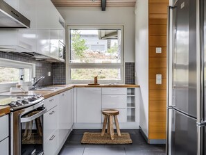 A modern kitchen with white cabinetry, a stainless steel refrigerator, and a window overlooking a residential area. - Rukavuorenhuippu 23 a by Interhome (Kuusamo)