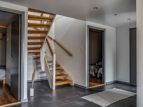 Et moderne interiør med en trappe i træ, en seng og en grå måtte.