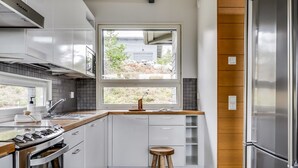 Een moderne keuken met witte kasten, een roestvrijstalen koelkast en een groot raam met uitzicht op de omgeving.