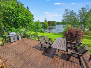 A deck with a grill, picnic table, and chairs overlooking a lake.