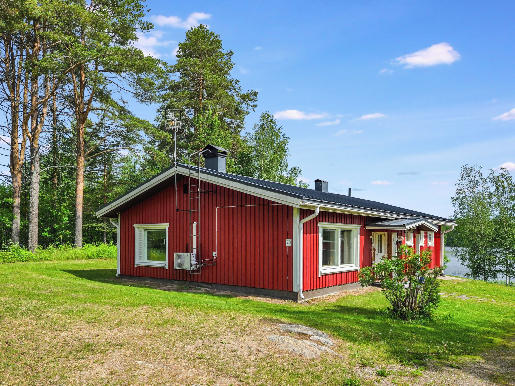 Une cabane rouge à un seul étage, dotée d’une cheminée et d’un petit porche avec une fenêtre.