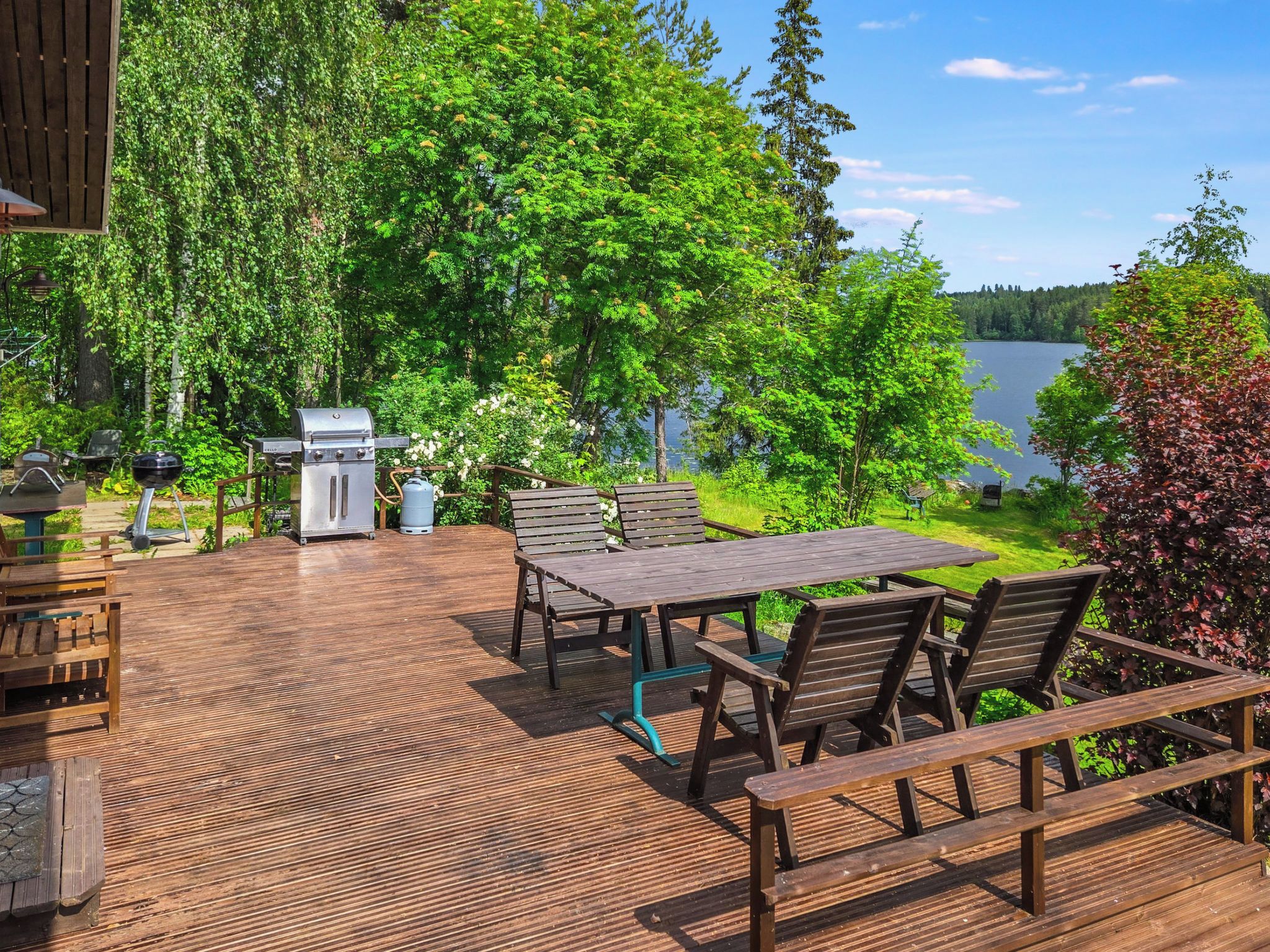 Eine Terrass mit Grill, Picknicktisch und Stühlen mit Blick auf einen See.