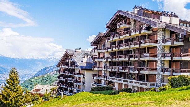 Ein mehrstöckiges Hotel mit Balkonen vor einer Bergkulisse.