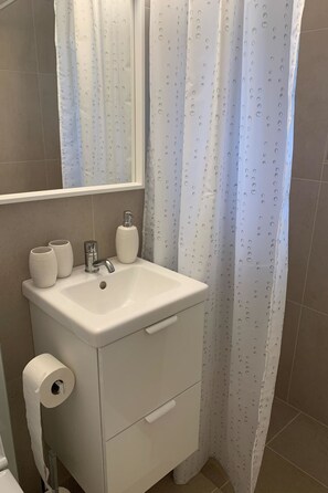 A bathroom with a white sink, a mirror above it, a toilet paper holder, and a shower curtain with a pattern. - Kitty (Parterre) by Interhome (Schönried)
