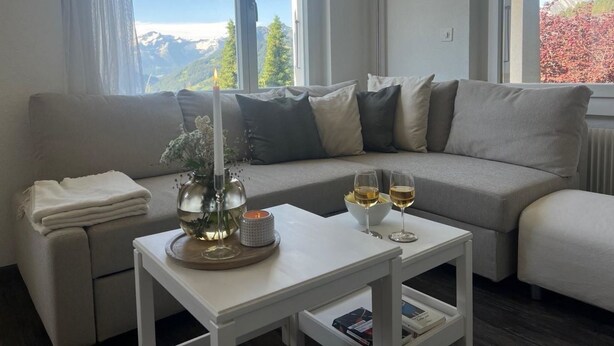 Uma sala de estar moderna com um sofá cinzento, uma mesa de centro branca e dois copos de vinho branco.