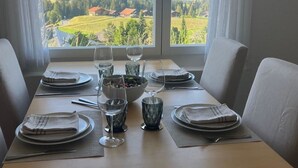 Mesa de jantar posta para quatro pessoas, com vista para as montanhas através de grandes janelas.