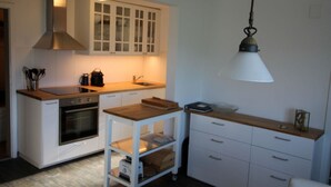Uma cozinha compacta com armários brancos, bancada de madeira, forno embutido e uma luminária pendente.