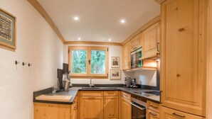 A kitchen with wooden cabinets, a black countertop, a window with a view of greenery, and a stove. - Les Silenes by Interhome (Gstaad)