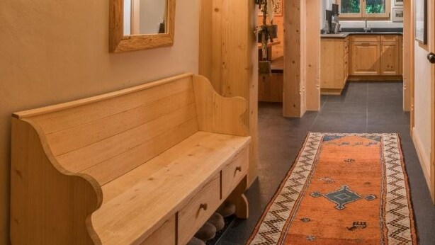 A wooden interior with a bench, a patterned rug, and a kitchen in the background. - Les Silenes by Interhome (Gstaad)