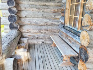 A log cabin with a wooden deck, benches, and a glass window.