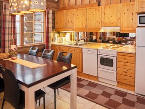 A wooden cabin-style kitchen with a dining table and chairs, wooden cabinets, a stove, and a microwave. - Kelovalta 7b by Interhome (Kuusamo)