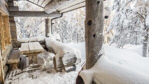 Eine rustikale Holzhütte mit einer Bank und einem Tisch, umgeben von schneebedeckten Bäumen.