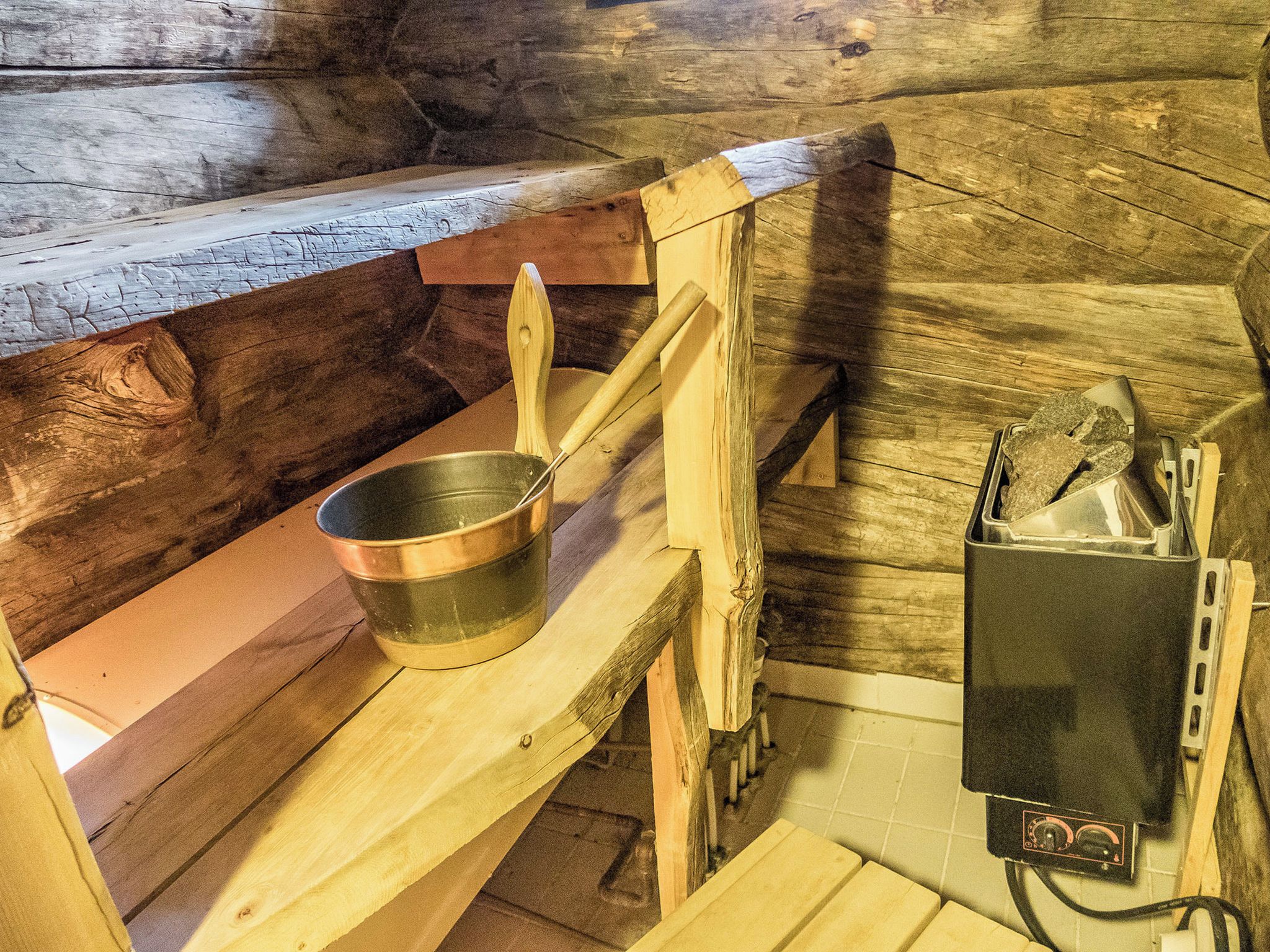 A rustic wooden sauna with benches, a metal bucket, and a heater.