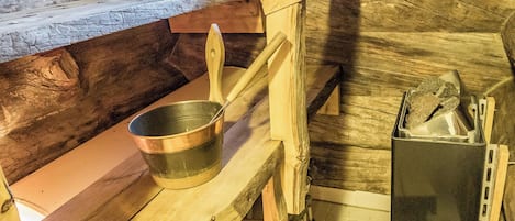 A rustic wooden sauna with benches, a metal bucket, and a heater.
