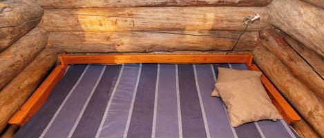 Una habitación tipo cabaña de madera con una cama, un ventanal y una mesita.