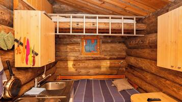 L’intérieur d’un chalet en bois compact comprend un lit superposé, une petite kitchenette et un meuble en bois contenant des ustensiles de cuisine.