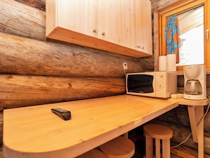 Innenansicht einer Holzhütte mit Küchenbereich, inklusive Mikrowelle, Kaffeemaschine und einer Fernbedienung auf einem Holztisch.