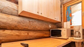 A wooden cabin interior with a kitchen area featuring a microwave, coffee maker, and a remote control on the counter.