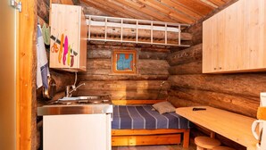 A compact log cabin room with a bed, a small kitchenette, and a wooden table with stools.