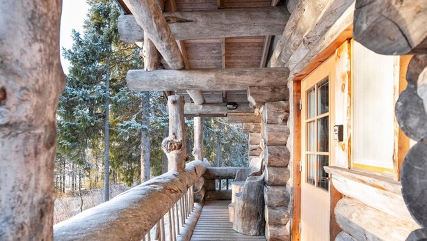 A log cabin with a wooden deck leading to a windowed porch.