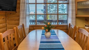 Comedor de cabaña de madera con un ventanal grande, una mesa con sillas y un florero con flores.