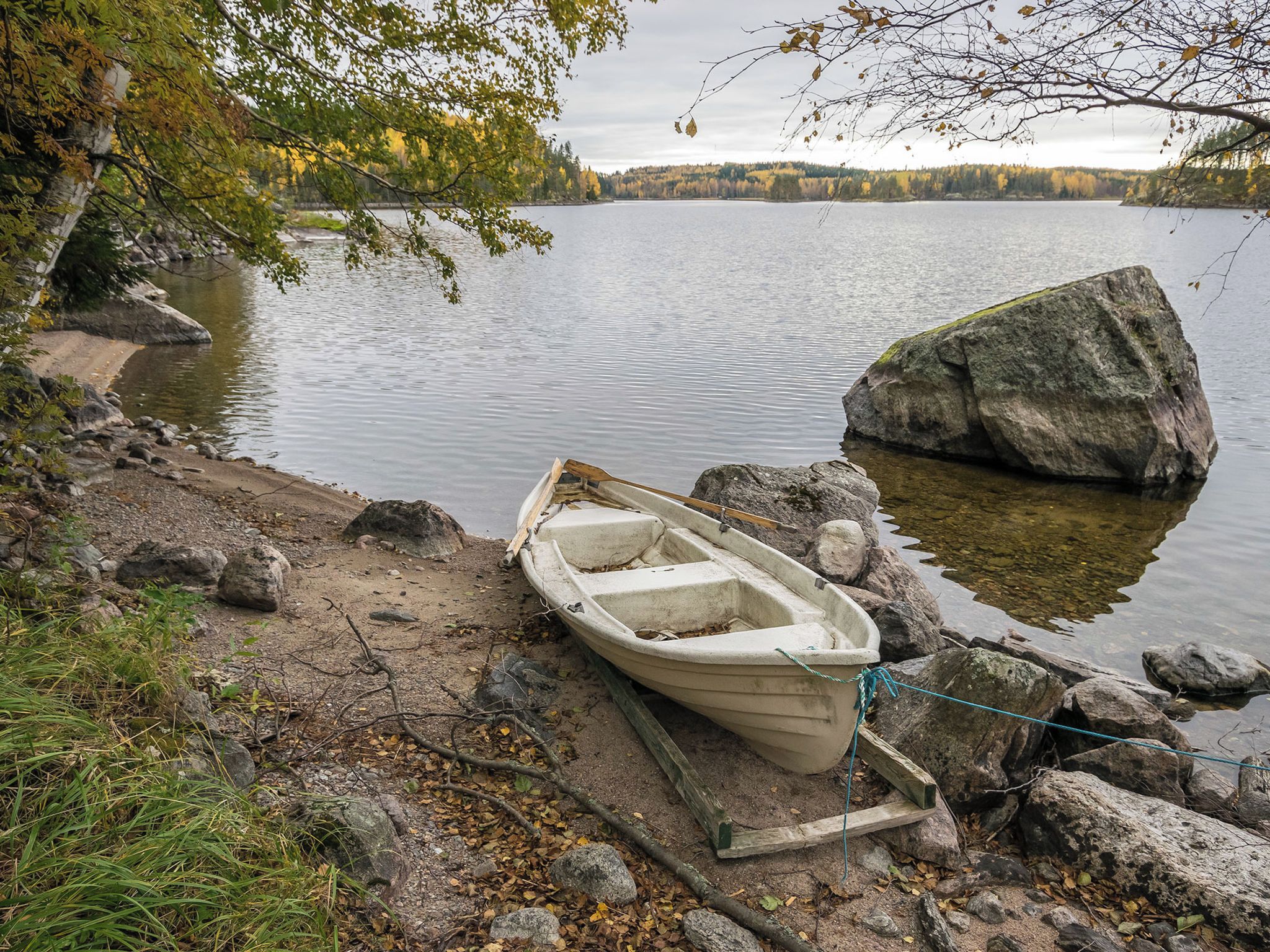 Una pequeña embarcación amarrada a una costa rocosa, con un lago tranquilo y un bosque al fondo.
