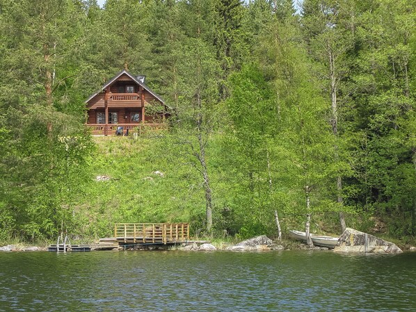A cabin with a deck overlooking a lake, surrounded by dense forest.