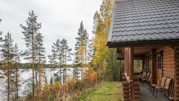 Una cabaña de troncos con porche y zona de estar al aire libre, con vista a un lago.