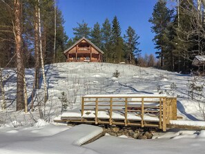A wooden cabin with a balcony, surrounded by snow-covered ground and trees.