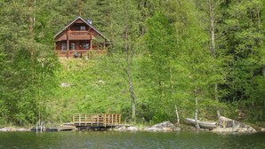 Una cabaña de madera con terraza, rodeada de un bosque denso y un lago.