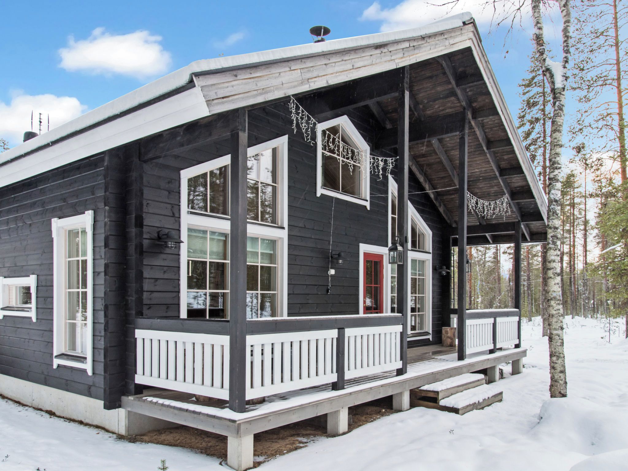 A wooden cabin with a porch, large windows, and a red door.