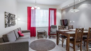 Un salon moderne avec un canapé gris, des rideaux rouges, une table à manger avec des chaises, un téléviseur et un tableau accroché au mur.