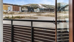 Blick vom Balkon auf einen Parkplatz mit Gebäuden und einer hügeligen Landschaft im Hintergrund.