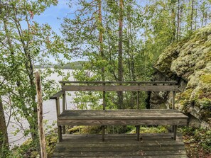 Un banco de madera con vista a un lago, rodeado de árboles y terreno rocoso.