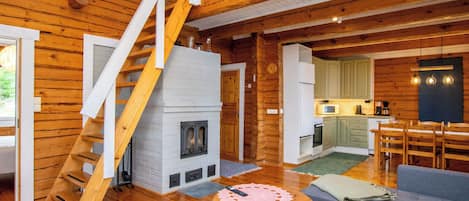Interior de una cabaña de madera con chimenea, escalera, cocina y zona de estar.