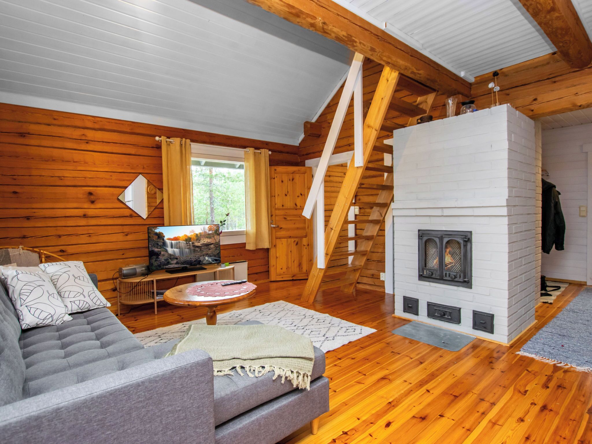 A log cabin interior with a fireplace, wooden walls, a sofa, and a television.