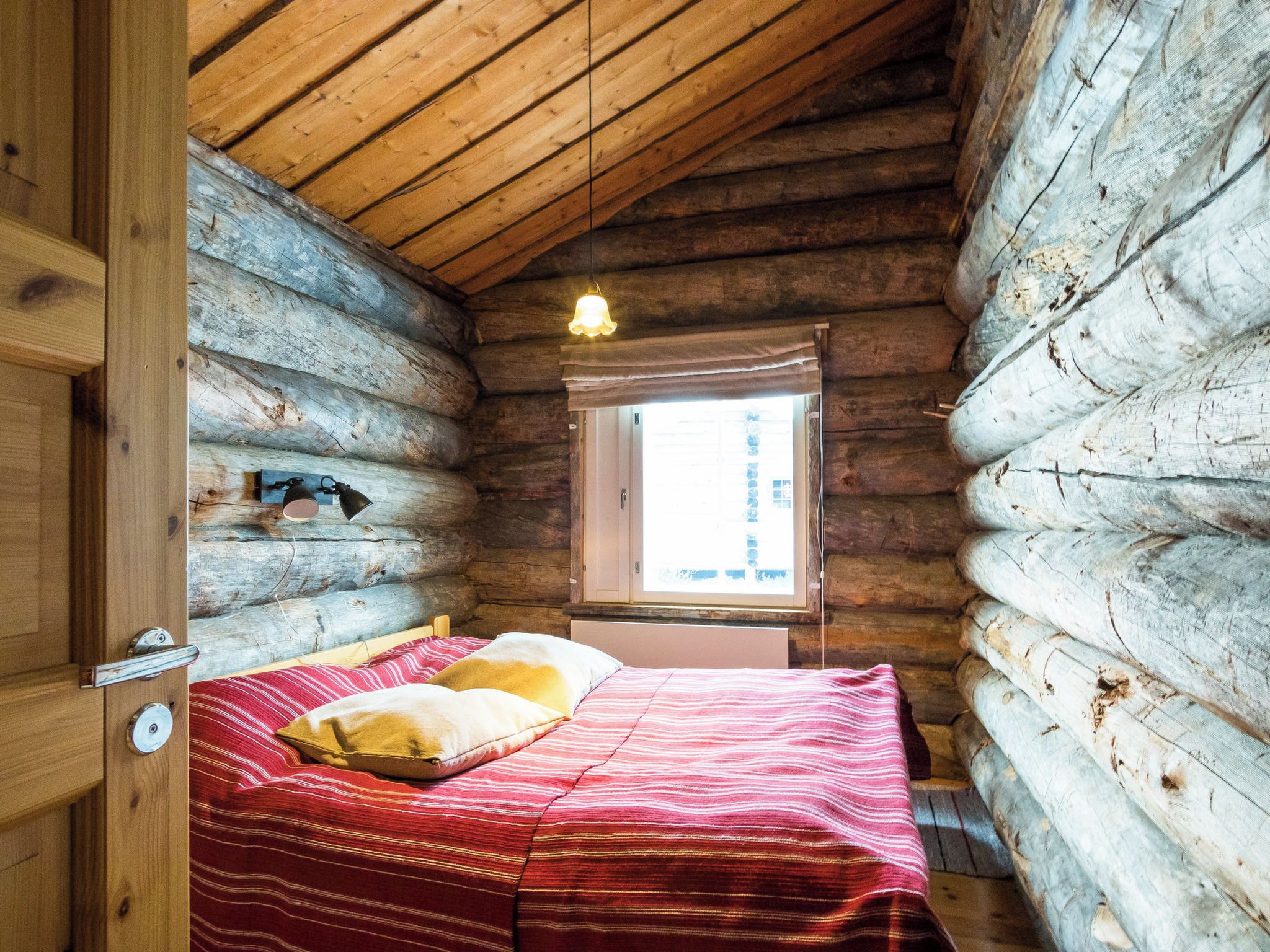 A log cabin bedroom with a bed, a window, and a hanging light fixture.