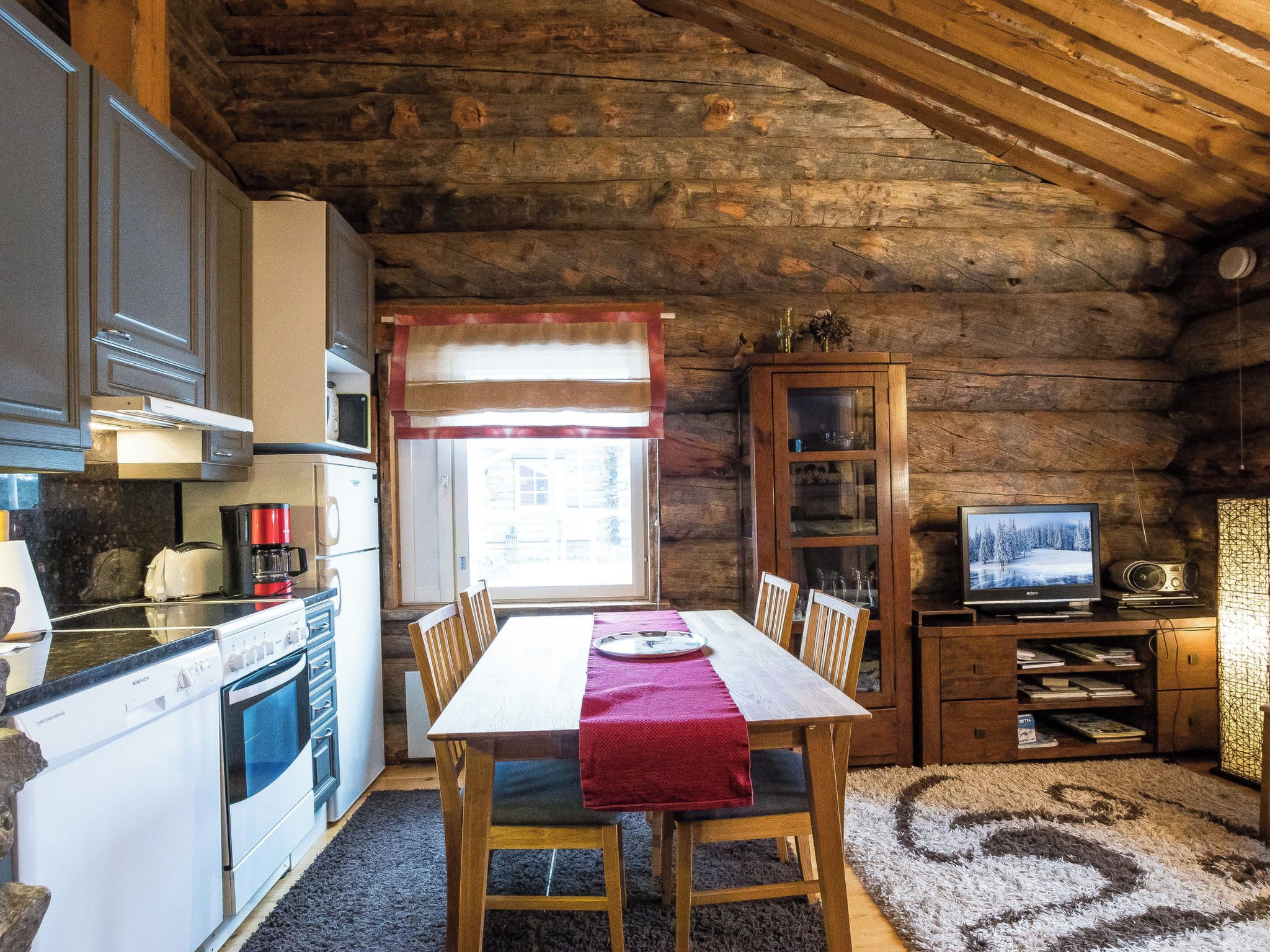 A rustic cabin interior with a kitchen, dining area, and a television.