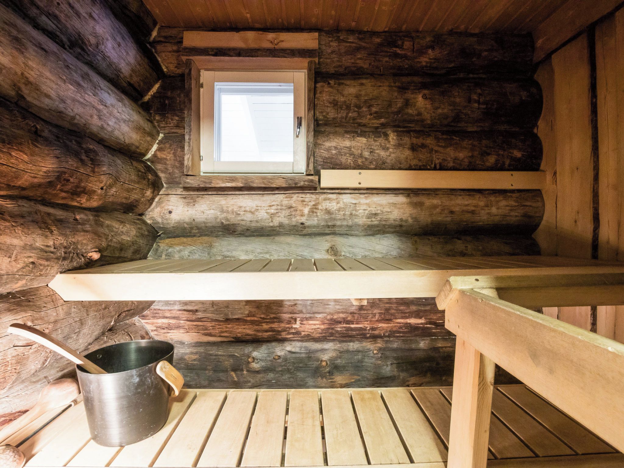 A log cabin interior with a window, a wooden bench, and a metal pot.