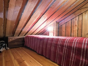 Ein Zimmer mit schrägverdeckter Decke, Holzwänden, einem Bett mit gestreifter Bettdecke und Holzboden.