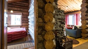 Interior de una cabaña de troncos con cama, sofá y pared de piedra.
