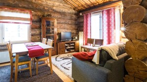 Interior de una cabaña de troncos con comedor, televisor y sofá.