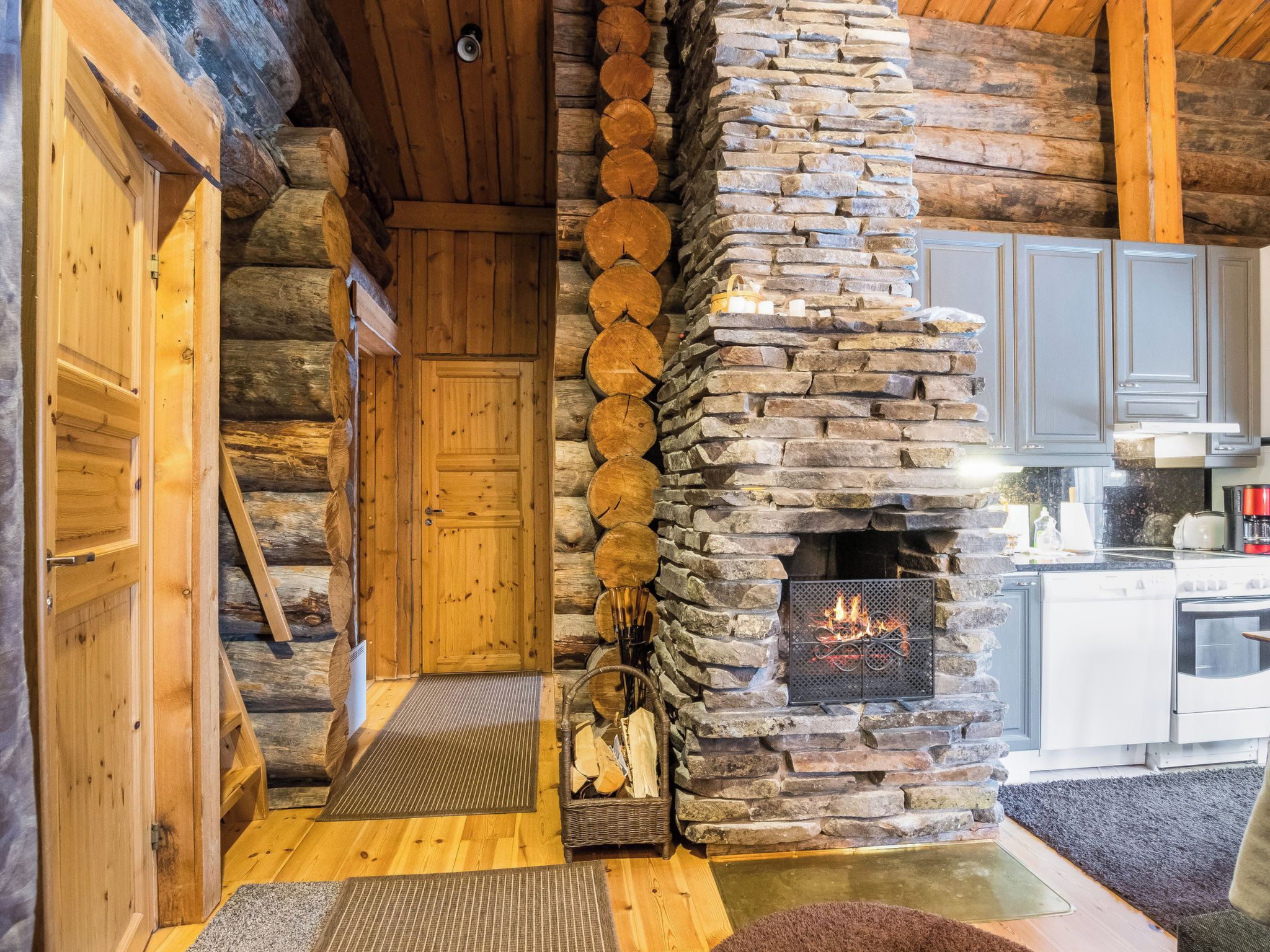 A log cabin interior with a stone fireplace, wooden door, and kitchen area.