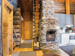 Ein Innenraum einer Blockhütte mit Kamin aus Stein, Holztür und Küchenbereich.