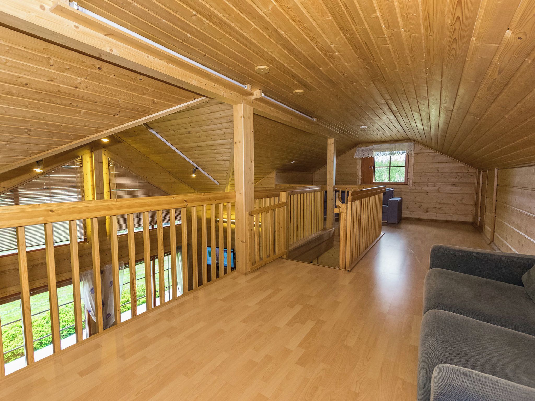 Une pièce mansardée spacieuse avec des poutres apparentes, un balcon et une vue sur la verdure environnante.